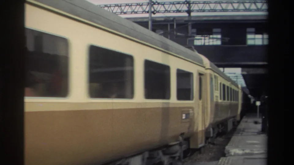 Cream-and-brown passenger coaches at a covered Taiwan railway station platform, circa 1982, with large passenger windows and overhead gantry structure, captured on 8mm.