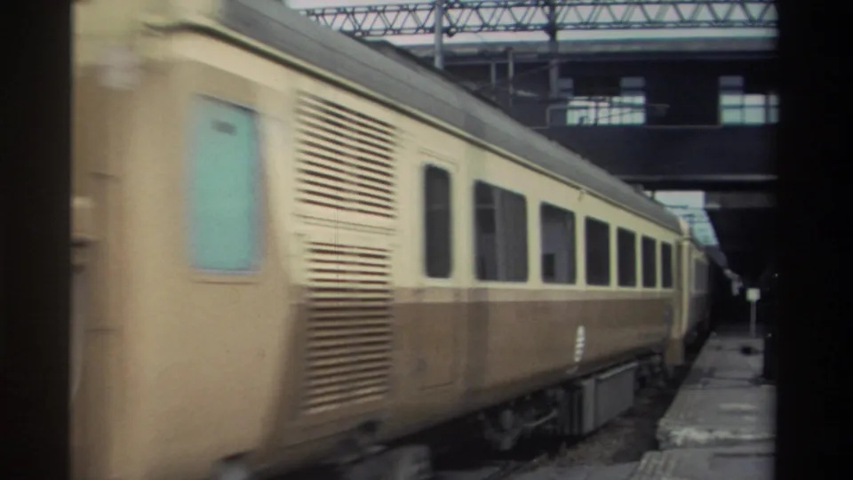 Motion-blurred cream-and-brown passenger coaches passing close to the stationary camera at a Taiwan railway station, circa 1982, with turquoise door panel, 8mm.