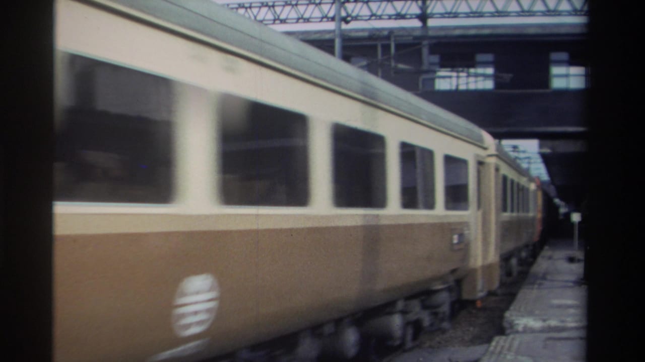 Two-tone cream-and-brown passenger train moving past a station platform in Taiwan, circa 1982, 8mm home movie footage.