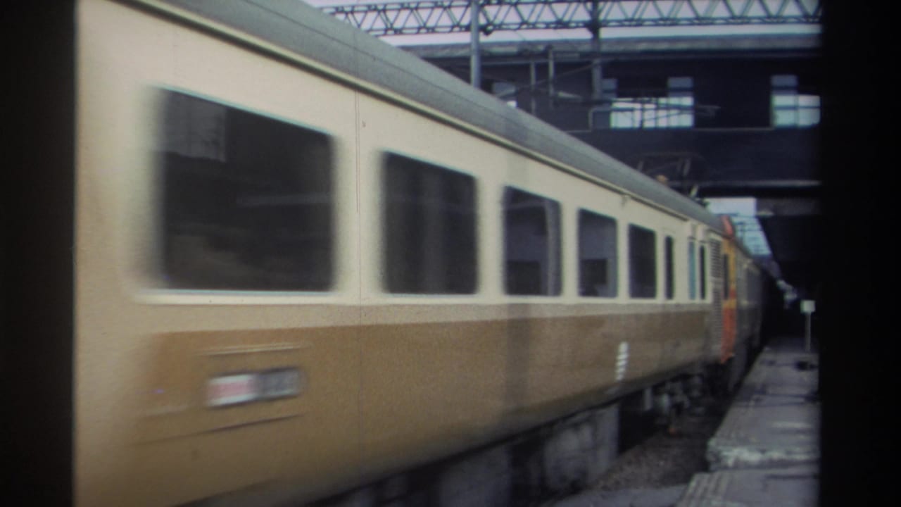 Cream-and-brown passenger cars moving past a station platform in Taiwan, circa 1982, with overhead rail infrastructure and a second train visible beyond.
