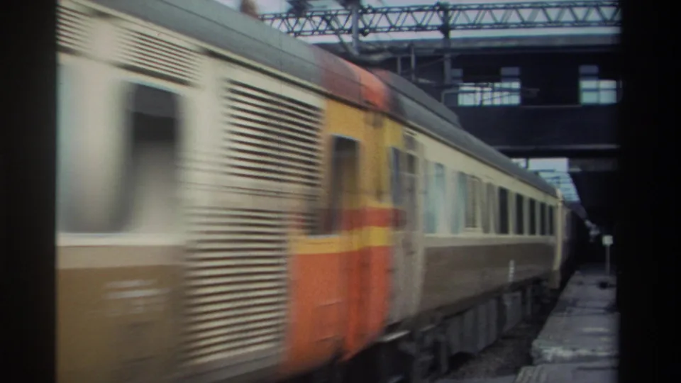 Orange locomotive or cab car and cream-and-brown passenger cars at a station platform in Taiwan, circa 1982, with heavy motion blur.