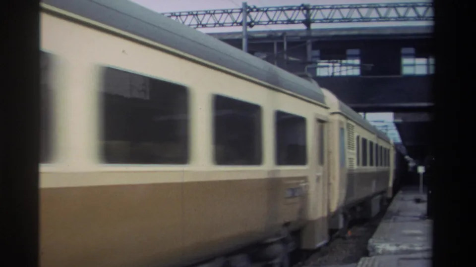Trailing section of a cream-and-brown passenger train at a station in Taiwan, circa 1982, with overhead catenary gantries and a small platform signal visible.