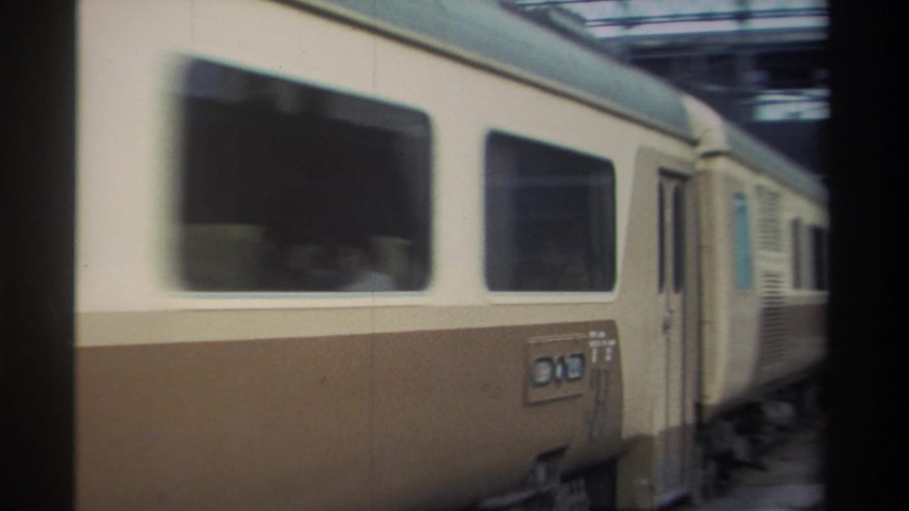 Close-up of cream upper and brown lower passenger railcar side showing large windows, ventilation panels, and a small unlegible placard.