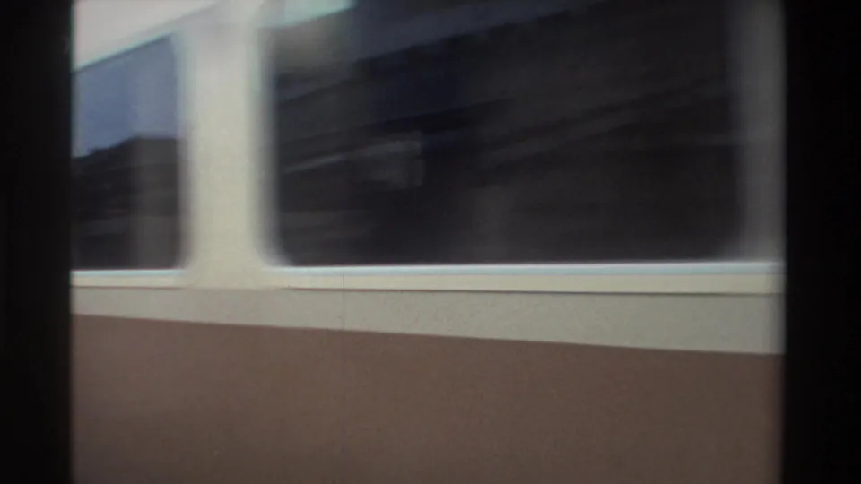 Handheld 8mm view of departing cream-and-brown passenger railcars pulling away from a covered station platform, Taiwan, circa 1982.