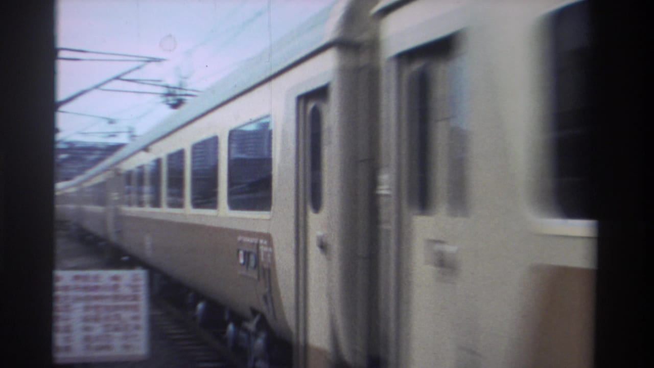 Close-up of a cream-and-brown striped passenger train car moving past the camera, with overhead electric wires at the top of the frame.