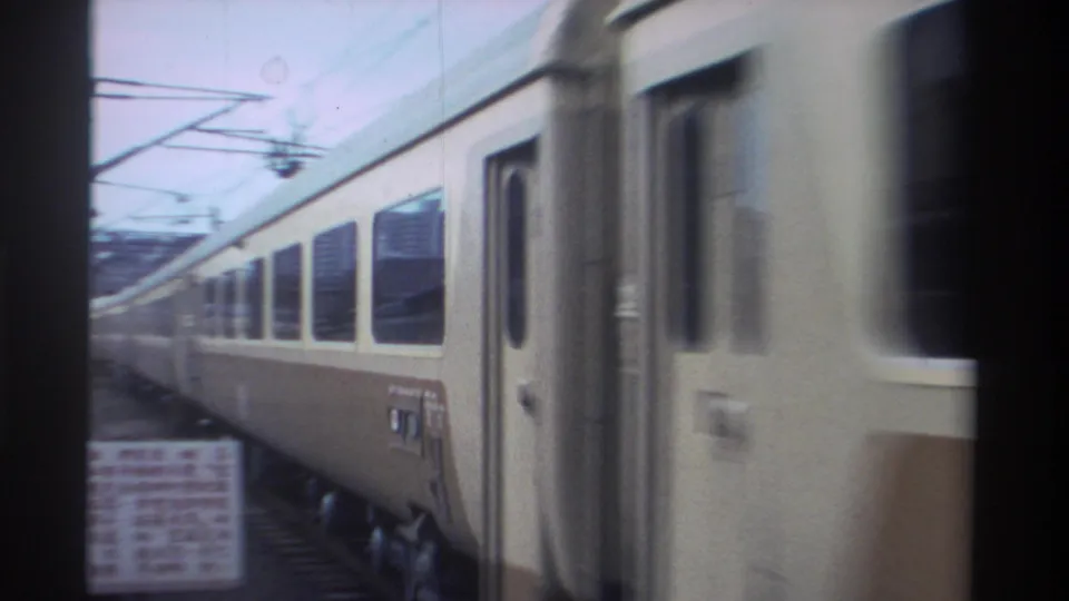 Close-up of a cream-and-brown passenger coach in motion at a Taiwan railway station, 1982, with catenary wires overhead and a partial Chinese-script sign at lower left.