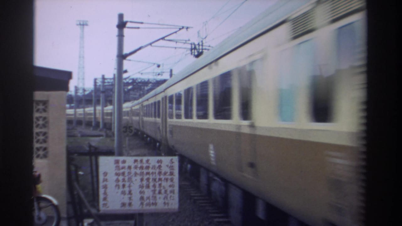 Side of a cream passenger train alongside station catenary poles, a white Chinese-script signage board on a post, and a parked bicycle.