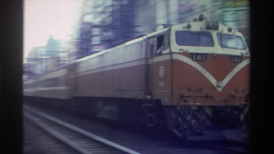 Close-range 8mm frame of locomotive E413 passing at speed with strong motion blur, orange livery dominant, Taiwan circa 1982.