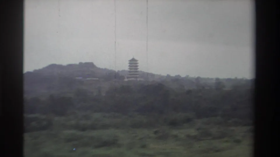 1982 Taiwan, 8mm film — pagoda and hillside landscape viewed from a moving vehicle; grey sky and lush vegetation prominent.