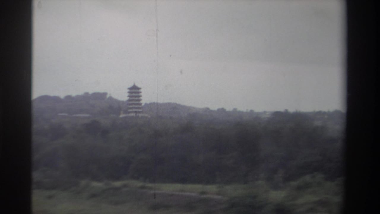 8mm home movie frame showing a distant multi-tiered pagoda rising above subtropical hillside vegetation in Taiwan, circa 1982.