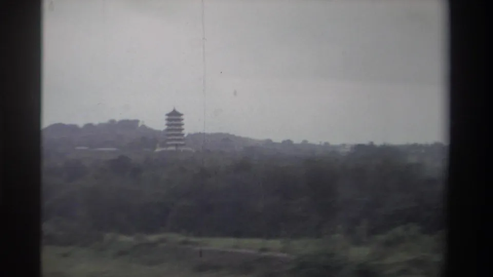 8mm home movie frame showing a distant multi-tiered pagoda rising above subtropical hillside vegetation in Taiwan, circa 1982.