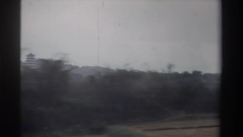 Closing 8mm frame from a moving vehicle in Taiwan, circa 1982; the pagoda remains visible above the treeline while the foreground blurs with motion.