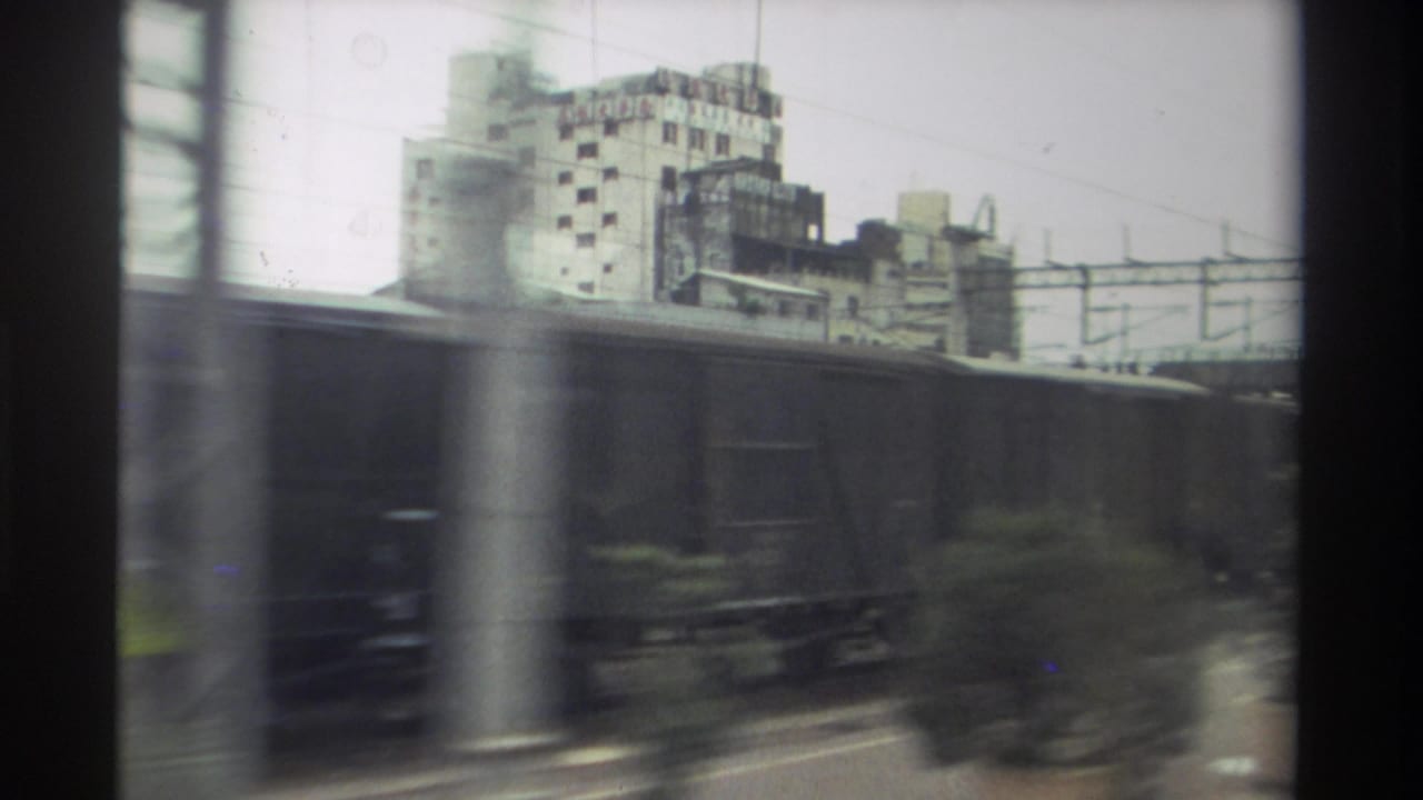 8mm home movie frame from Taiwan, 1982 — freight wagons blur past a moving train window with urban buildings and catenary wires behind.