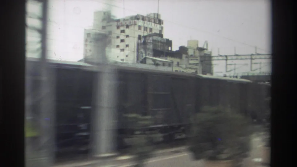 8mm home movie frame from Taiwan, 1982 — freight wagons blur past a moving train window with urban buildings and catenary wires behind.