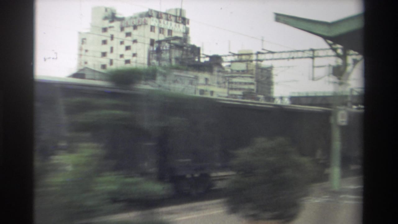 8mm home movie from Taiwan, 1982 — goods wagons continue past with a concrete urban building and trees visible through the carriage window.