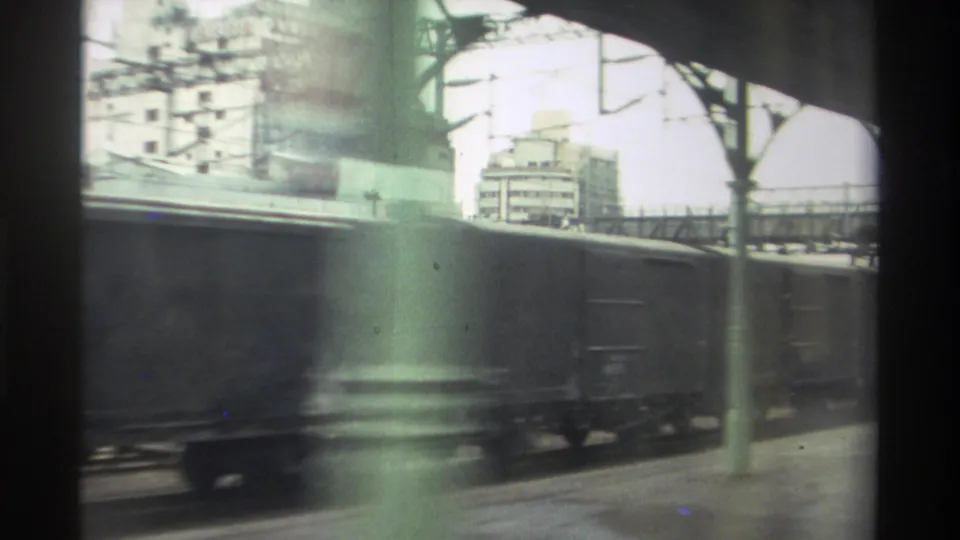8mm home movie from Taiwan, 1982 — green overhead rail infrastructure and painted pillars fill the frame as freight wagons pass beneath.