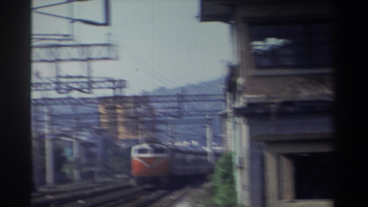 Orange-and-white Taiwan Railways locomotive approaching under a concrete overpass at speed, trackside 8mm home-movie footage, Taiwan, 1982.