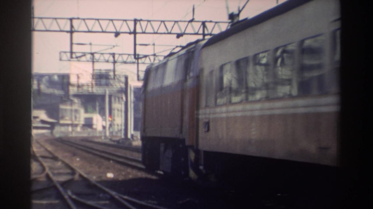 Cream-and-brown electric passenger train passing on outdoor tracks beneath overhead wires.