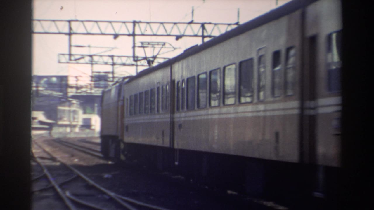 A cream-and-brown electric rail car passes through a Taiwan track area in bright daylight, with catenary structures overhead.