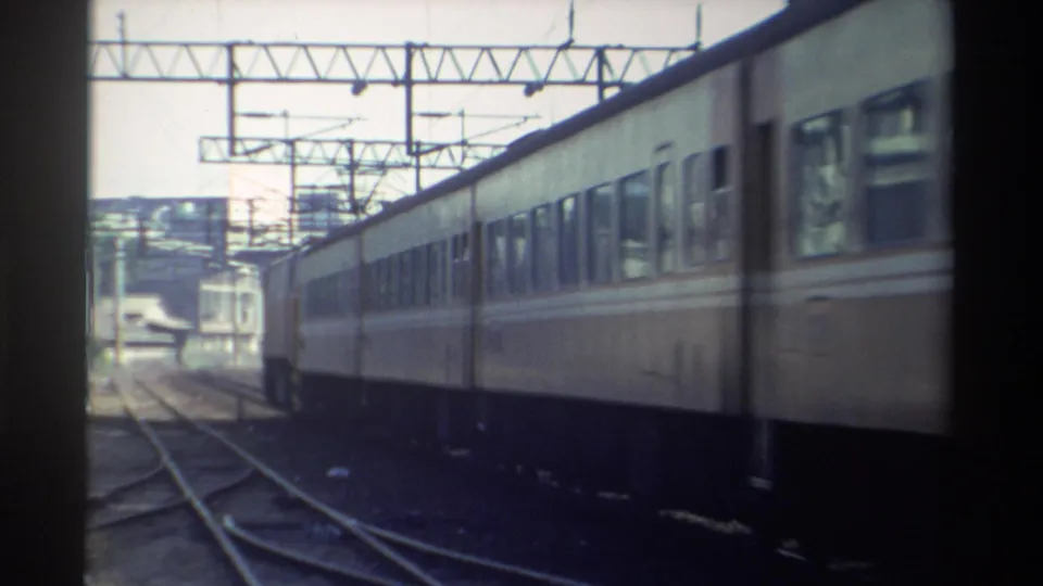 1982 Taiwan home-movie frame of a long electric passenger car moving beside visible switch tracks and overhead power supports.