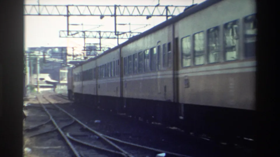 The passing electric train is seen farther down the outdoor rail line in Taiwan, framed by tracks, switches, and overhead wires.