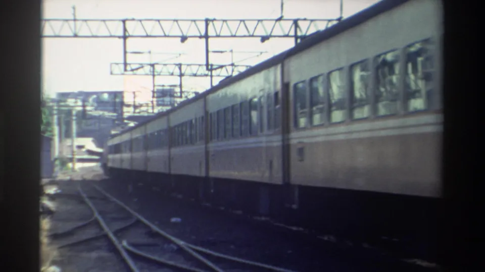 The train moves farther down the tracks in a 1982 Taiwan rail scene, framed by overhead electrical structures and film borders.