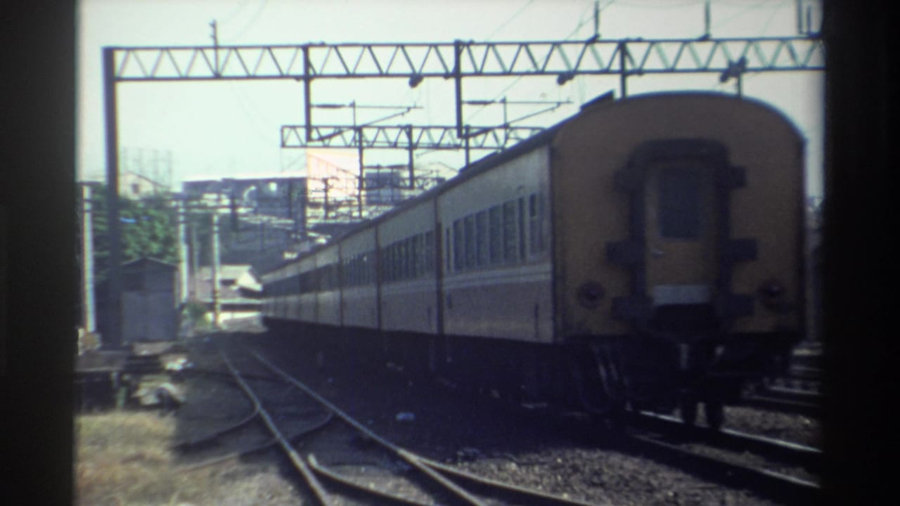 Rear of a passenger train receding along tracks below iron gantries.