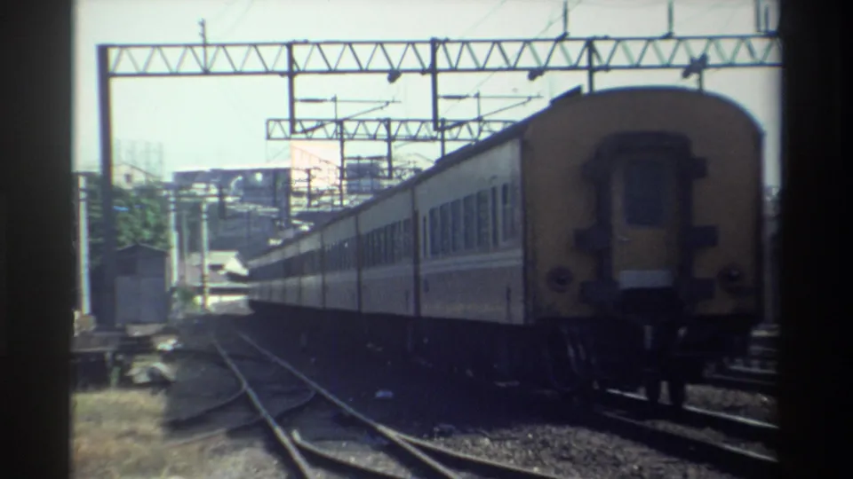 1982 Taiwan 8mm frame with the yellow rear of a passenger train moving away under overhead rail wires.