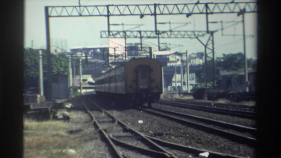 1982 Taiwan 8mm frame with the train further away amid multiple rails, gantries, and urban-edge structures.