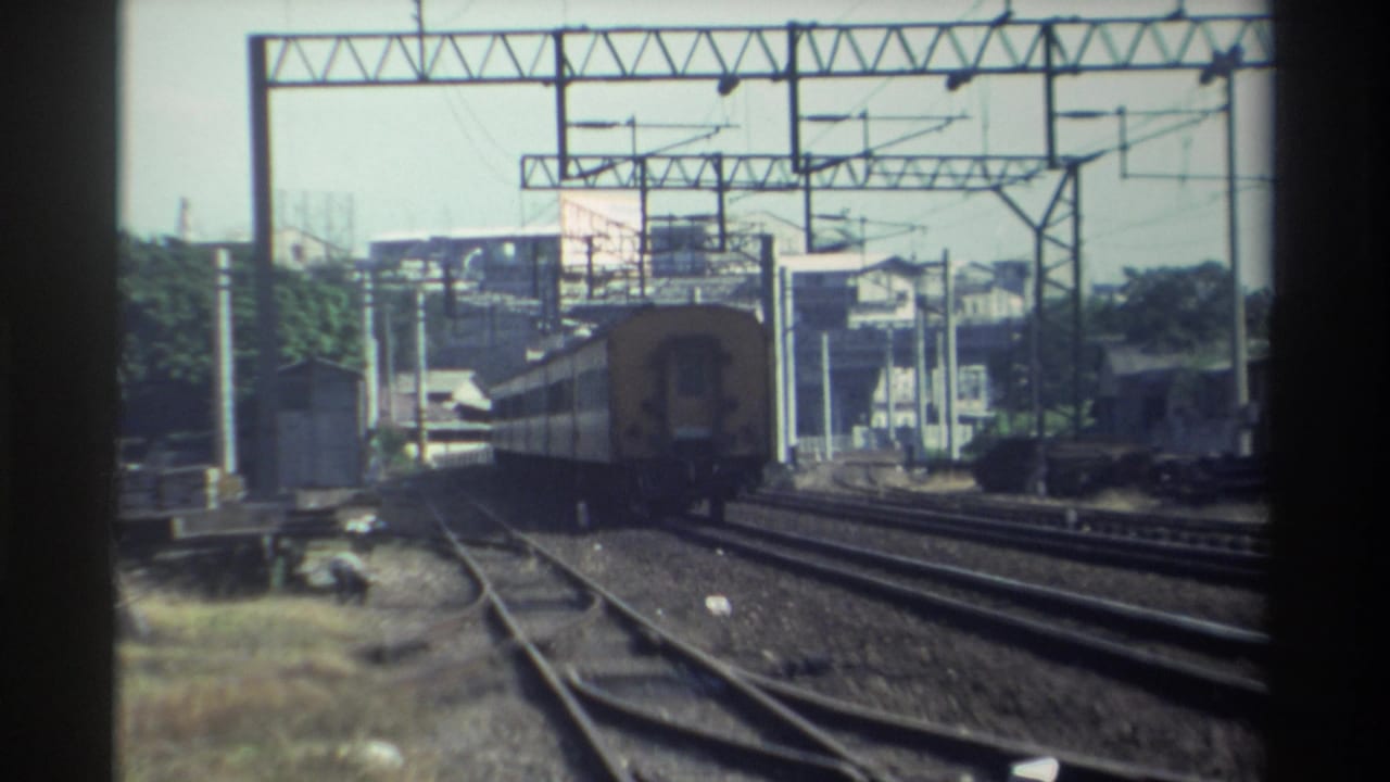 Yellow-and-cream train moving away on multiple railway tracks under overhead wires.