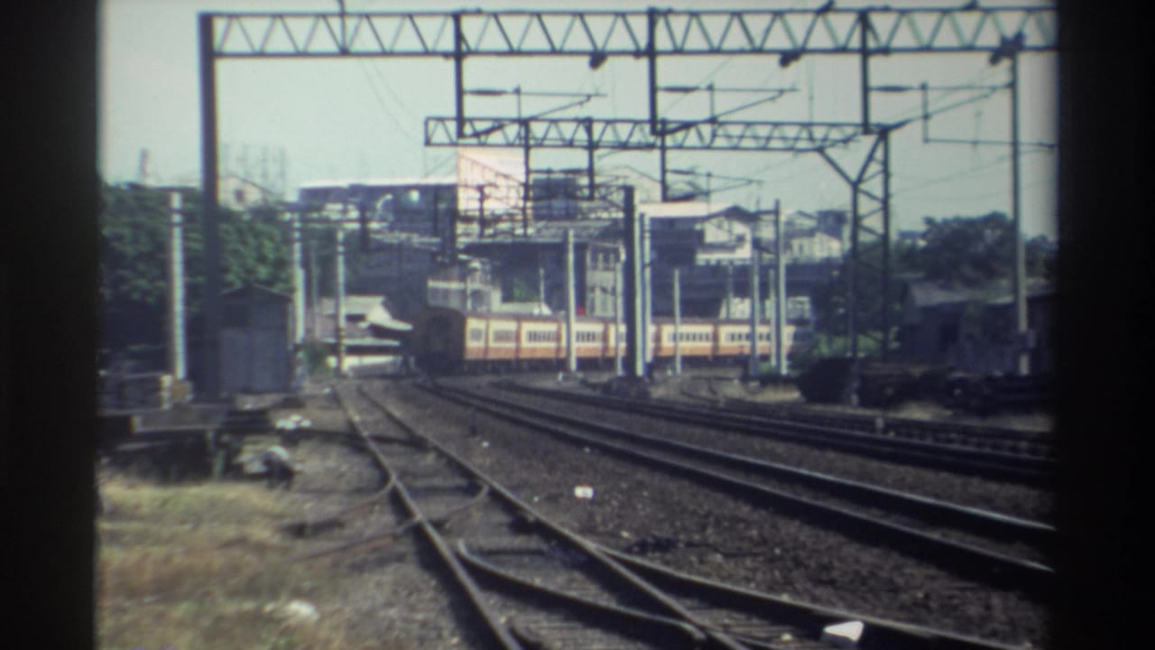 1982 Taiwan home-movie frame showing a cream-and-red passenger train on parallel tracks under overhead rail wires.
