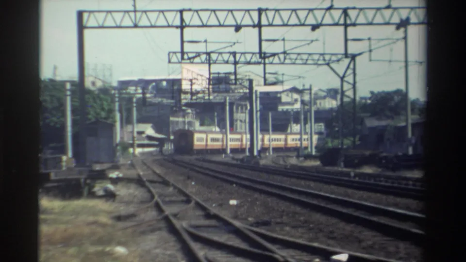 Cream-and-red passenger train continues through a Taiwan rail corridor, framed by catenary structures and soft 8mm edges.