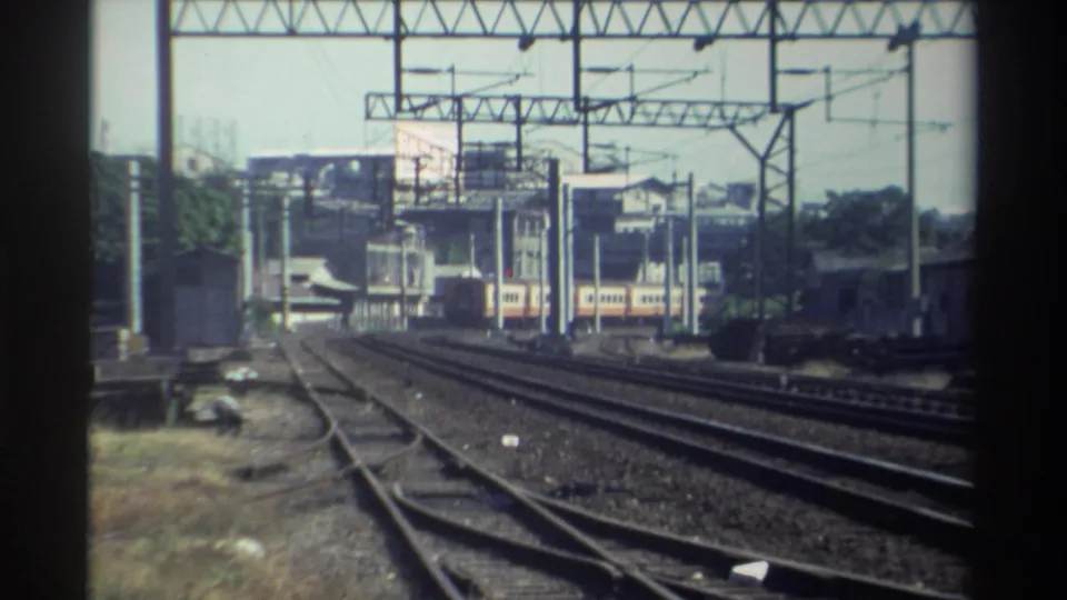Final 1982 Taiwan home-movie frame with the train receding amid tracks, catenary gantries, buildings, and faded film color.