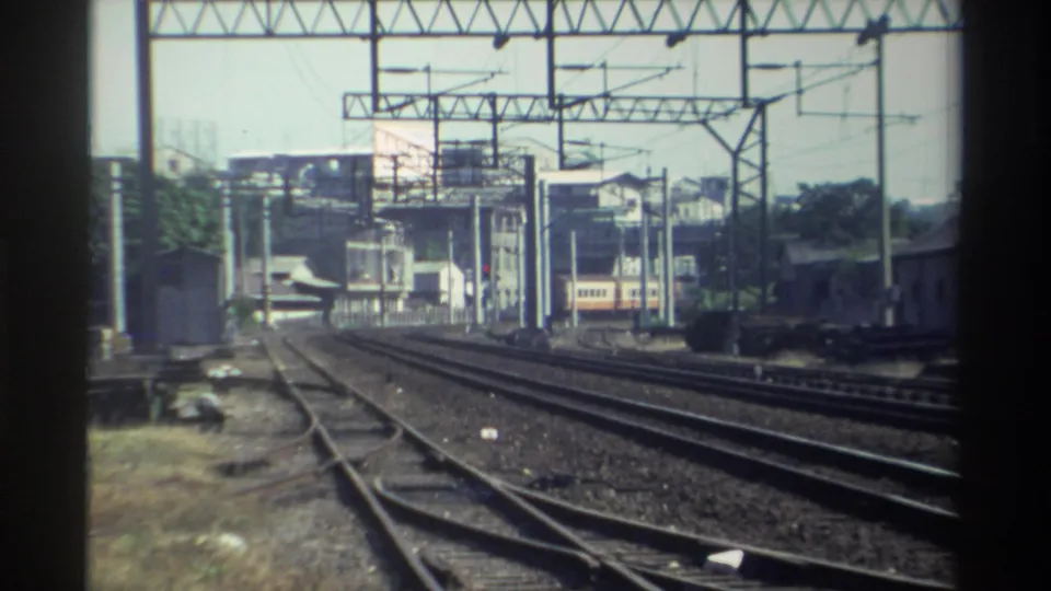 Home-movie frame from Taiwan in 1982 showing rail switchwork, parallel tracks, overhead lines, and a train in the background.