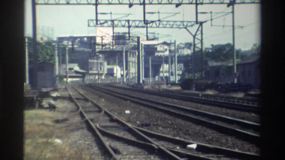 1982 Taiwan rail approach view from a moving train, with switching rails, overhead gantries, and station-area buildings visible.