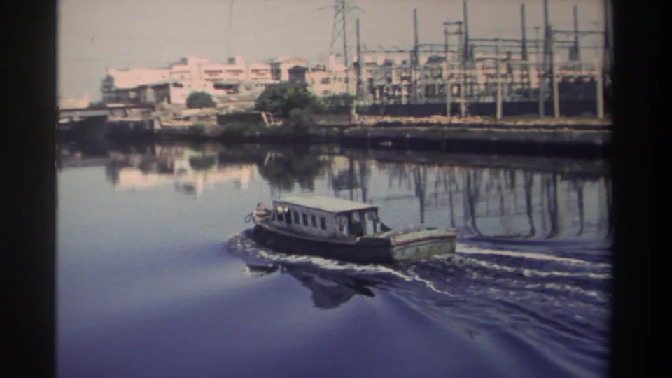 1982 Taiwan river view with a small motorboat passing near bridge spans, waterfront buildings, and a visible electrical substation.