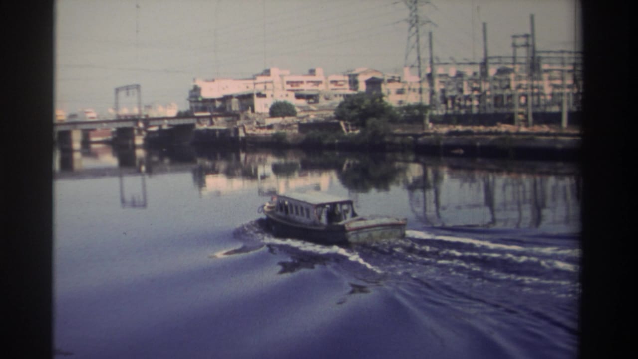 1982 Taiwan river view with a small motorboat passing below bridge infrastructure and an urban-industrial shoreline.