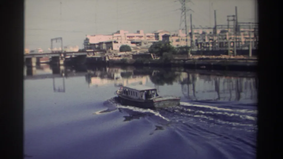 1982 Taiwan river view with a small motorboat passing below bridge infrastructure and an urban-industrial shoreline.