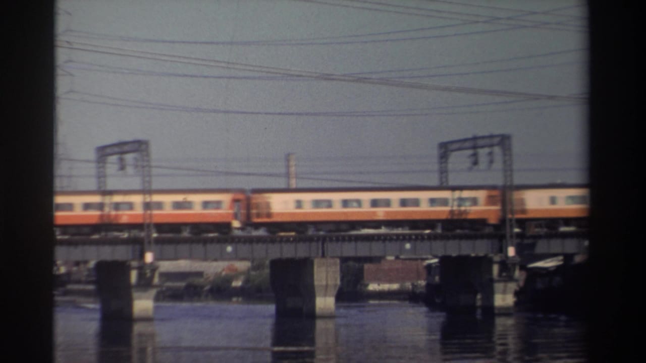 Passenger train crossing a bridge over water with overhead wires and concrete piers.