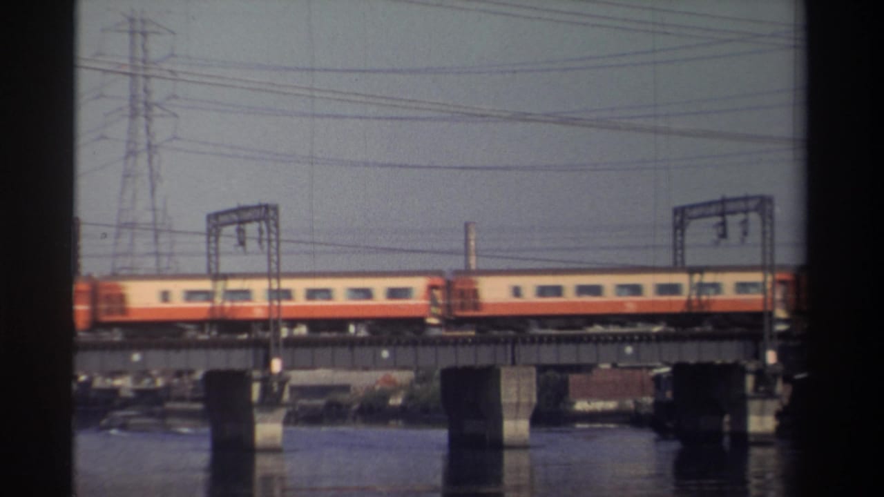 Orange-and-cream train cars on a bridge with water below and a utility tower behind.