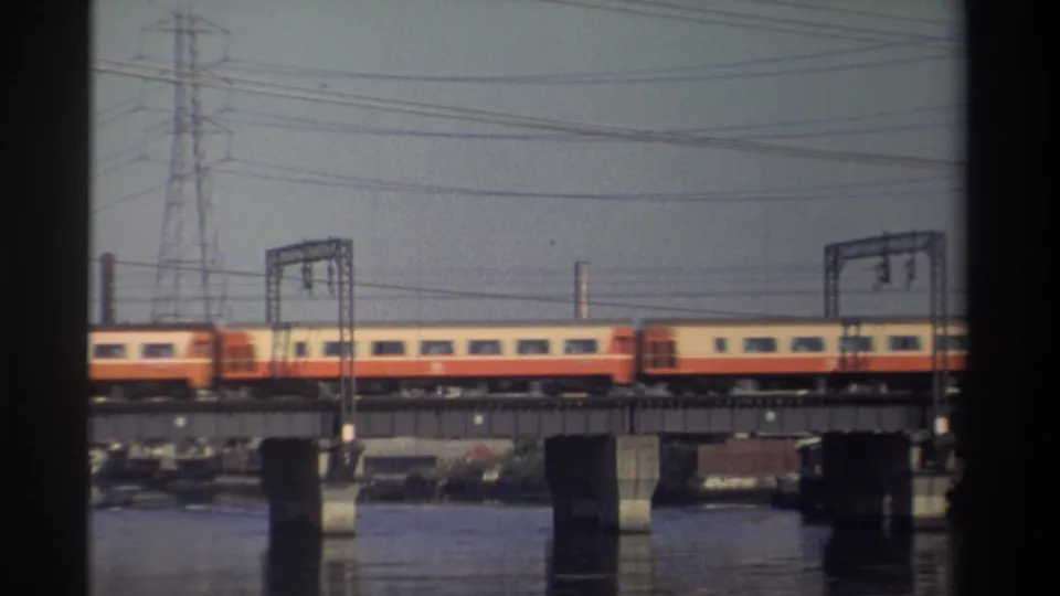 Late frame of the 1982 Taiwan rail crossing, showing train cars, bridge supports, overhead wires, and water below.