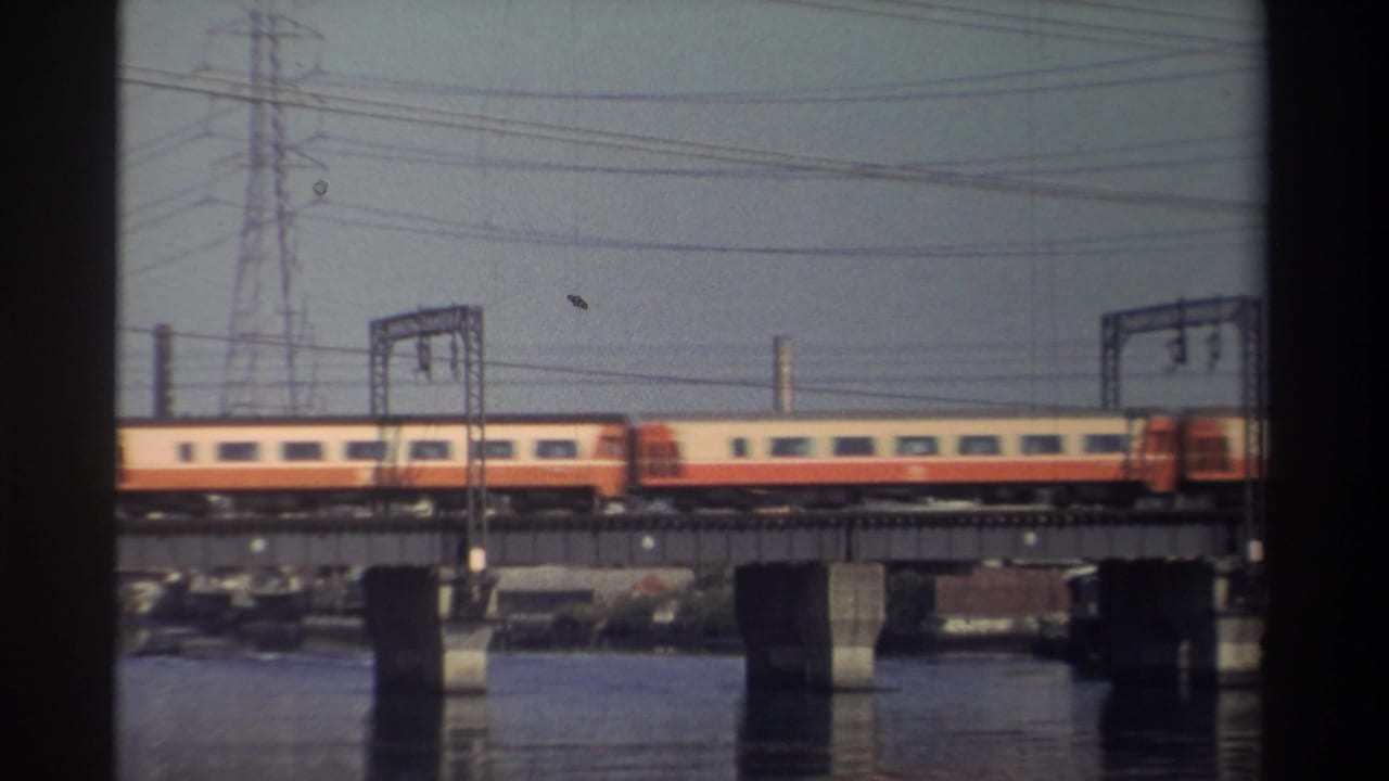 Yellow-and-red train crossing a bridge over water with power lines above.