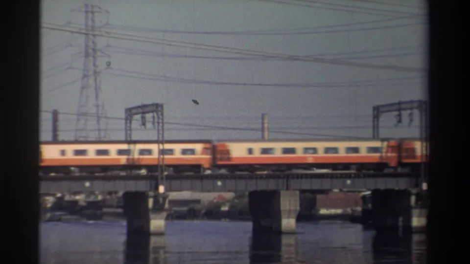 1982 Taiwan home-movie frame showing a yellow-and-red train moving across a concrete bridge over calm water.