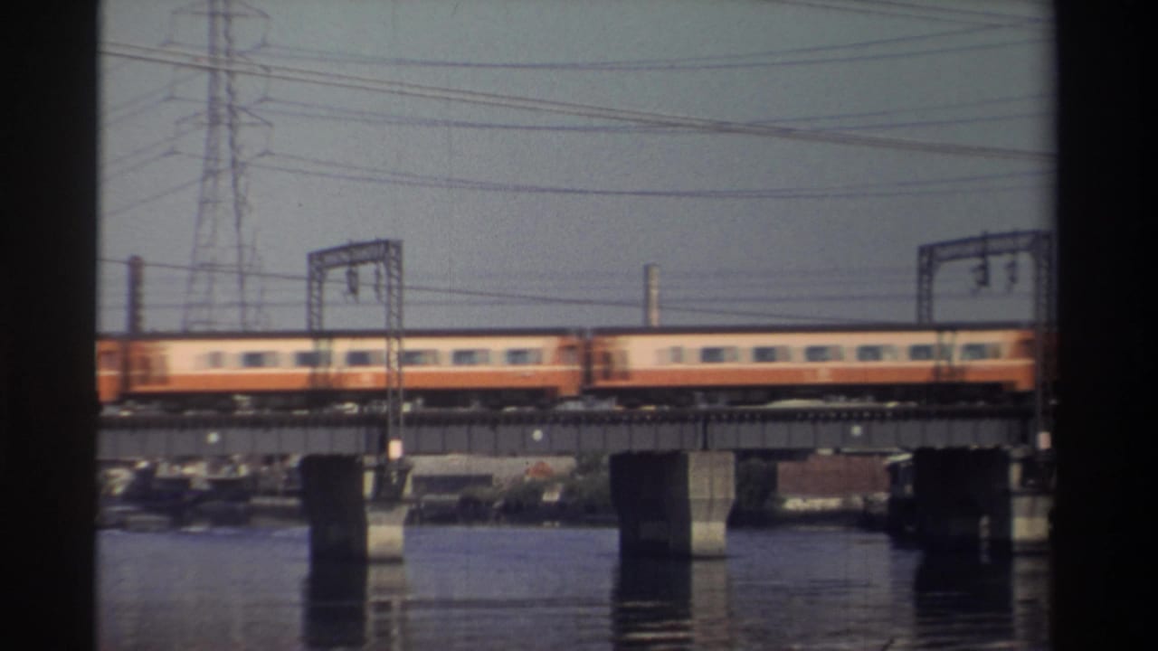 Train cars pass along a bridge with reflections on the water below.