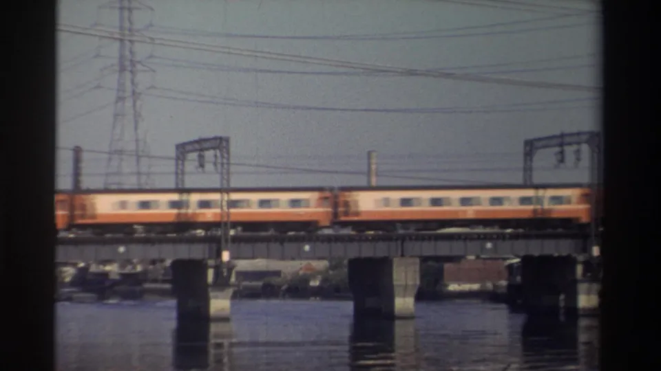 1982 Taiwan frame of yellow-and-red rail cars traveling across a bridge, with water and power infrastructure visible.