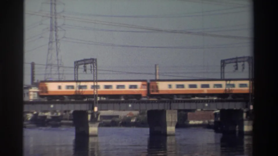 1982 Taiwan home-movie still showing rail cars centered on a bridge over water with utility structures behind.