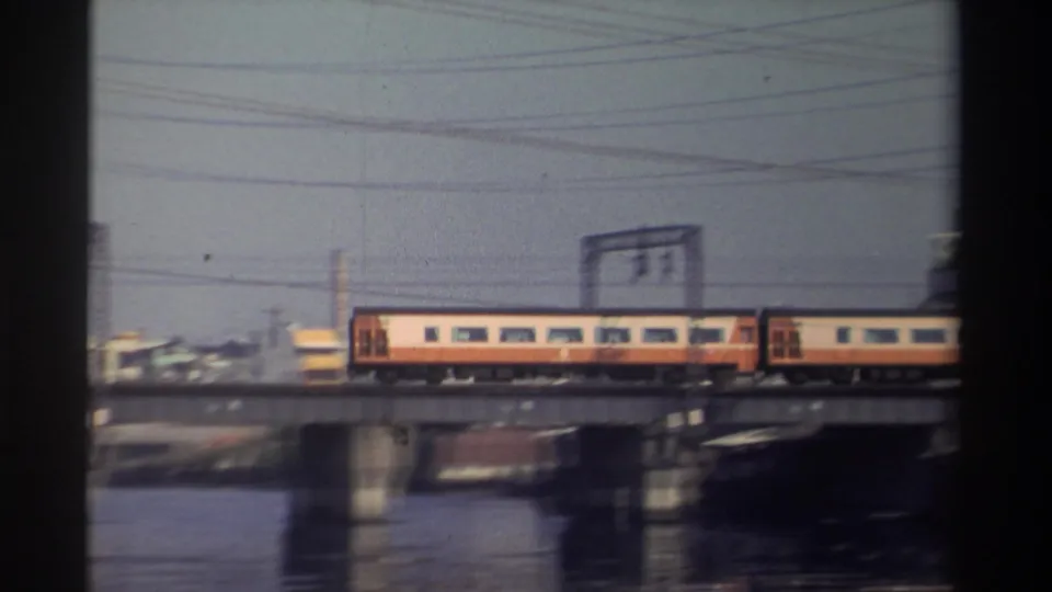 Final 1982 Taiwan frame showing the rear portion of a yellow-and-red train leaving the bridge view over water.