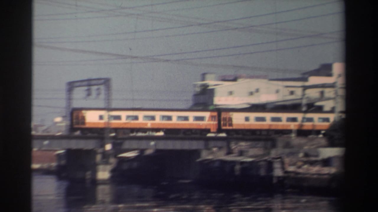 Cream-and-orange train crossing a bridge past industrial buildings and overhead wires.