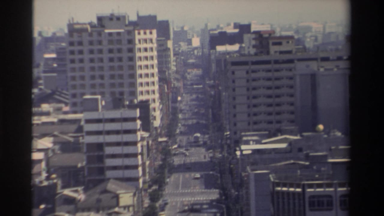 1982 Taiwan home-movie frame showing an elevated view of a straight urban avenue, mid-rise buildings, rooftops, and light traffic.