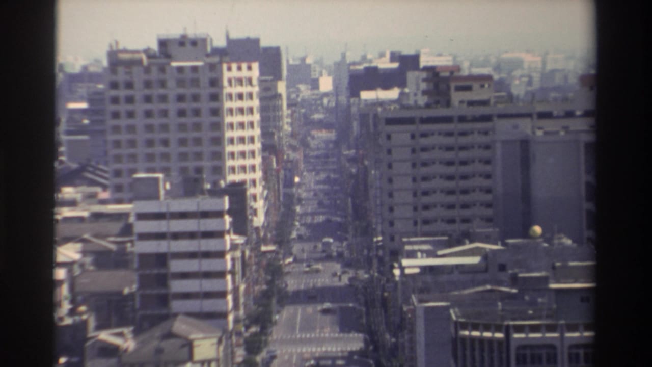 1982 Taiwan urban view from above, with a long avenue, concrete building facades, scattered vehicles, and hazy daylight.